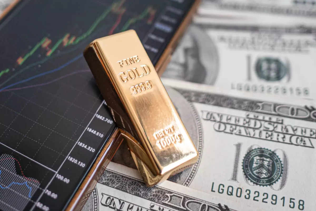 Gold bar on top of $100 bills and cellphone with stock graph